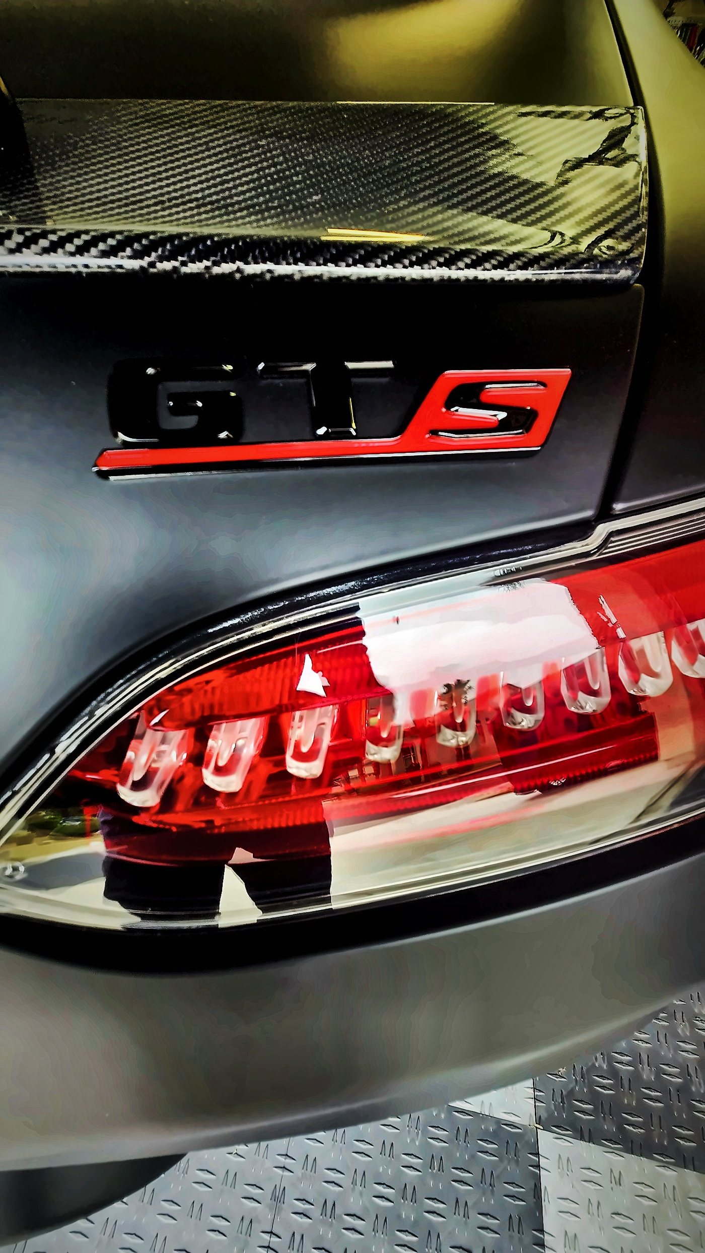 Gloss black and red GT S badge above a red LED taillight, with the carbon fiber rear wing