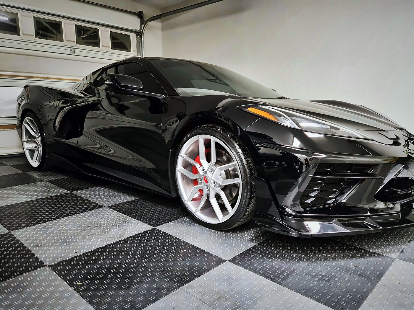 The black Corvette Stingray from the front three-quarter angle in a garage with a checkered floor